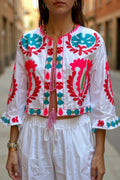 Chaqueta corta blanca de algodón de Iciar y Candela by Creasur S.L. con bordados florales fucsia y turquesa, mangas acampanadas y cordón.